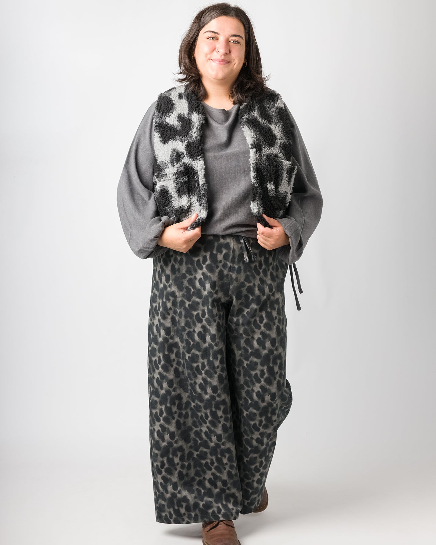 Flores trägt auf dem Foto 'Greta' mit Ballonärmel Größe XL, EcoVeroLeinen grau, 'Waltraut' Größe XXL/XXXL, Plüsch 'Dark Leobert' und 'Holly' weites Bein Größe XXL, Muster elastisch 'Dark Leobert'