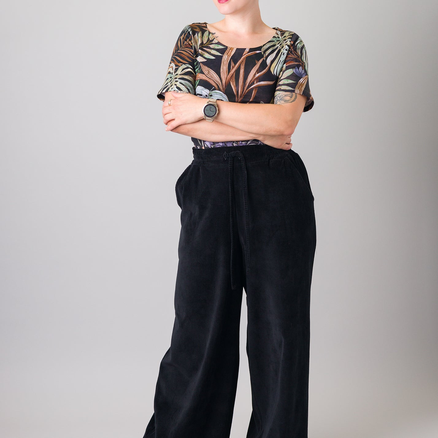 Melly trägt auf dem Foto 'Conni' kurzarm Größe S, Muster elastisch 'Plantlover' und 'Holly' weites Bein Größe XS, Velvet-Cord schwarz