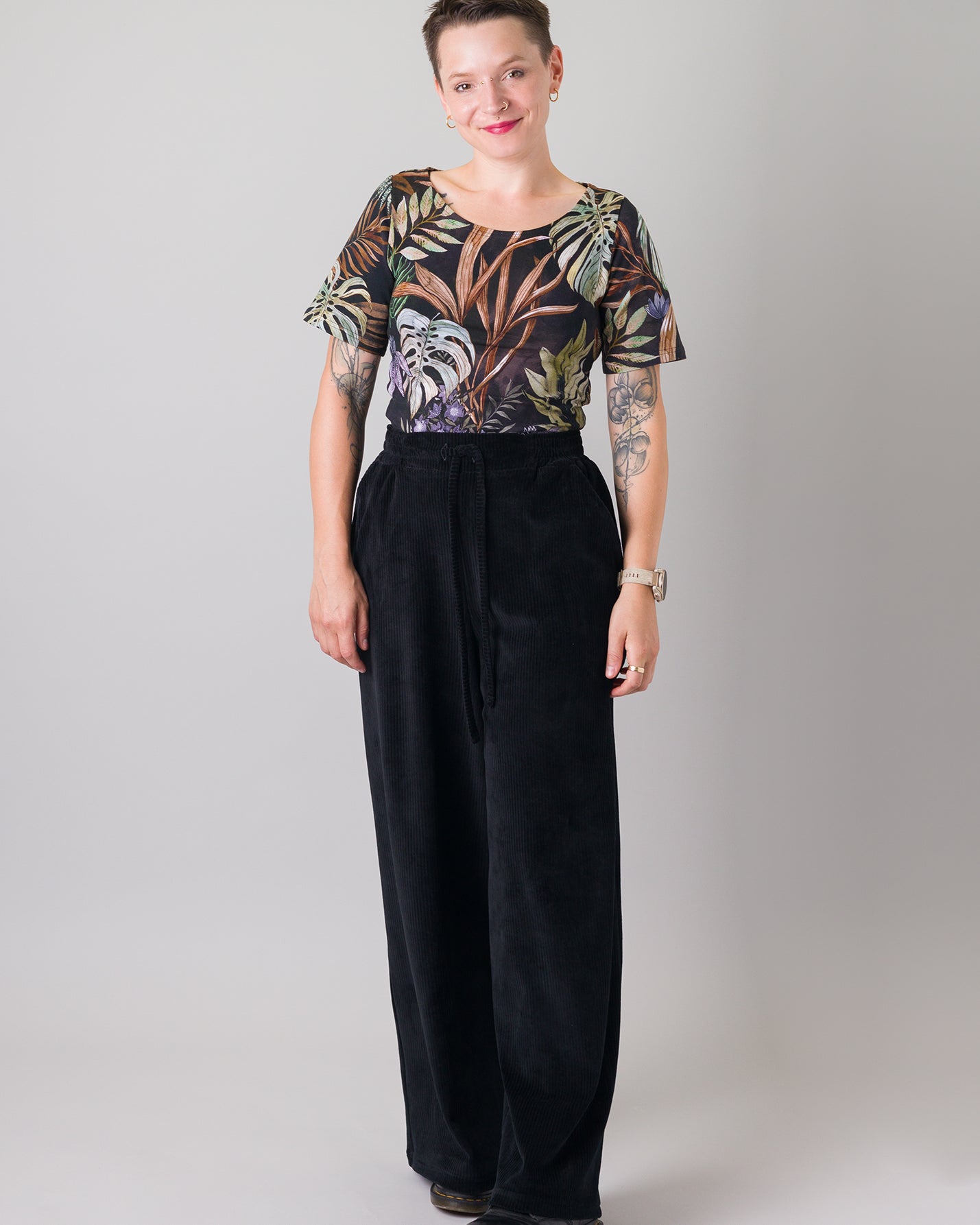 Melly trägt auf dem Foto 'Conni' kurzarm Größe S, Muster elastisch 'Plantlover' und 'Holly' weites Bein Größe XS, Velvet-Cord schwarz