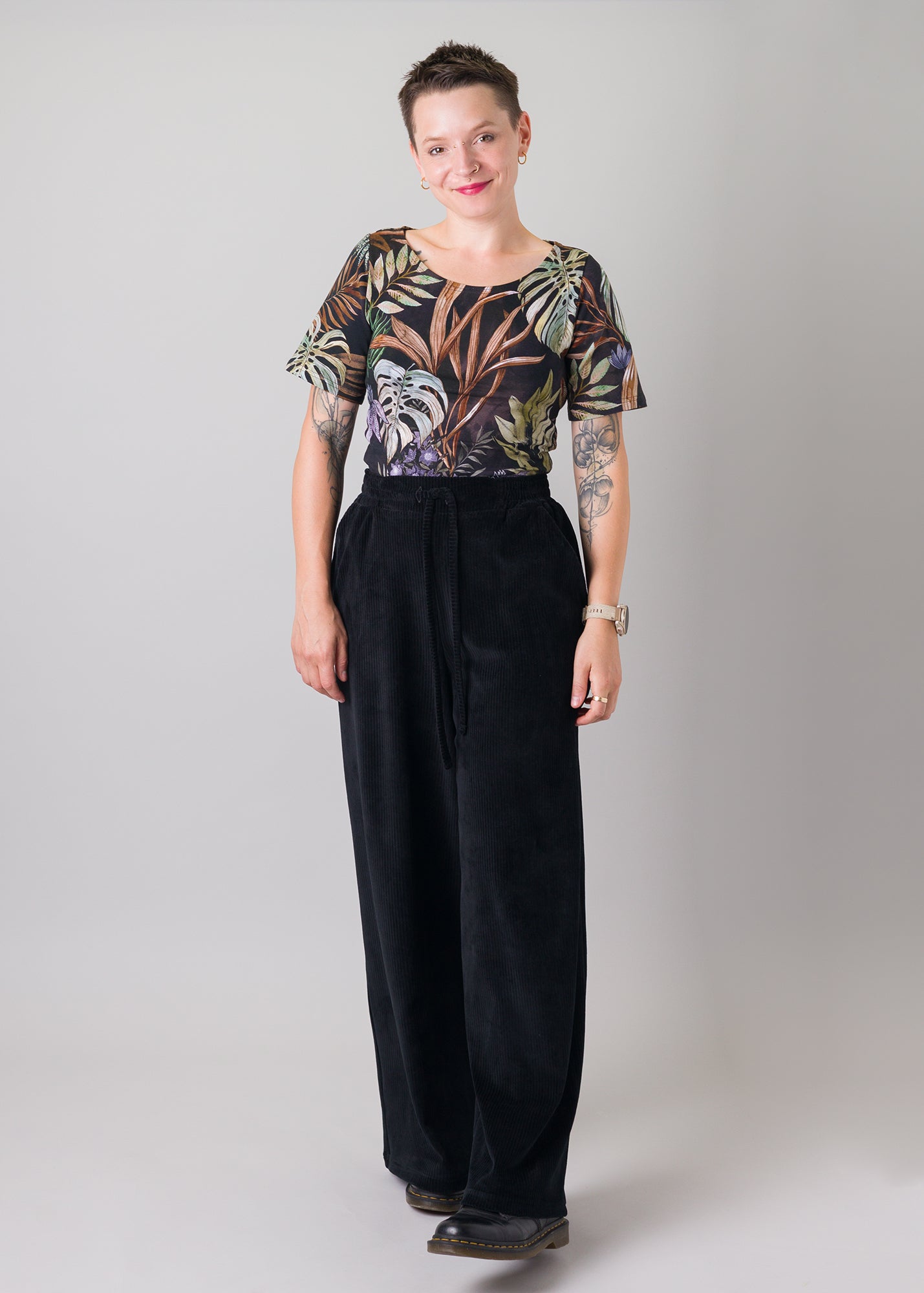 Melly trägt auf dem Foto 'Conni' kurzarm Größe S, Muster elastisch 'Plantlover' und 'Holly' weites Bein Größe XS, Velvet-Cord schwarz